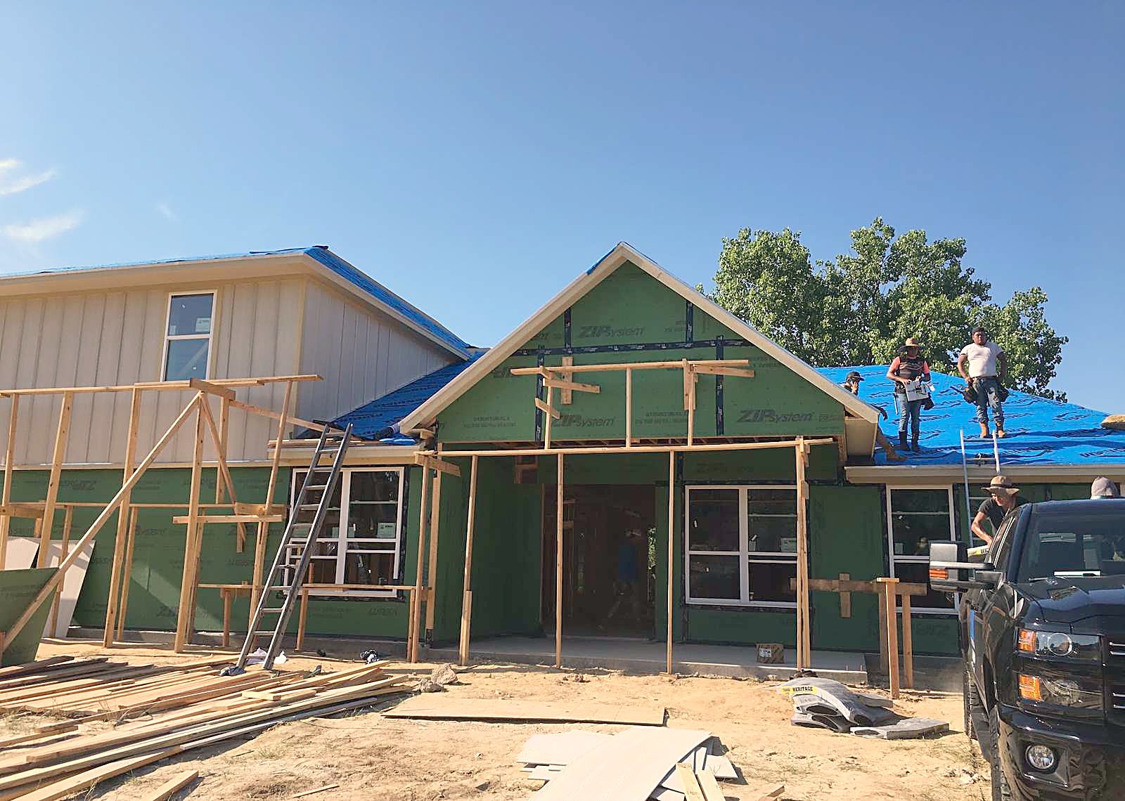 A roofing crew working on a new house with blue underlayment down over the decking